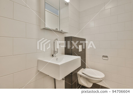 Wall hung toilet and small sink in corner in lavatory room with beige tile 94706604