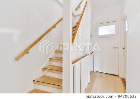 White spiral stairway connecting levels of contemporary house with wooden floor and white walls 94706632