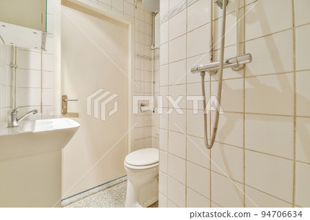 Flush toilet located between sink and shower in small tiled bathroom of contemporary apartment 94706634