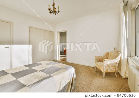 Comfortable bed with white bedclothes and bedside table with lamp placed near window and balcony door in light bedroom at home Comfortable bed with white bedclothes and bedside table with lamp placed near window and balcony door in light bedroom at home 94706636