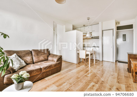 Contemporary minimalist style interior design of light studio apartment with wooden table and chairs in dining zone between open kitchen and living room with white walls and parquet floor Contemporary minimalist style interior design of light studio apartment with wooden table and chairs in dining zone between open kitchen and living room with white walls and parquet floor 94706680