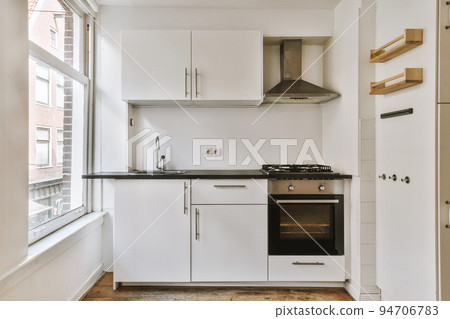 Well organized small home kitchen interior with sink under window and light furniture with stove and fridge in urban apartment 94706783