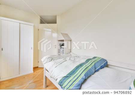 Home interior design of bedroom with bed and wooden wardrobe placed in corner near window in modern apartment 94706892
