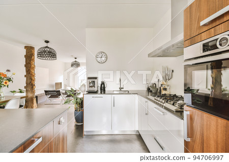 Modern minimalist style interior design of studio apartment with open white kitchen and dining zone with table and chairs illuminated by loft style lamp 94706997