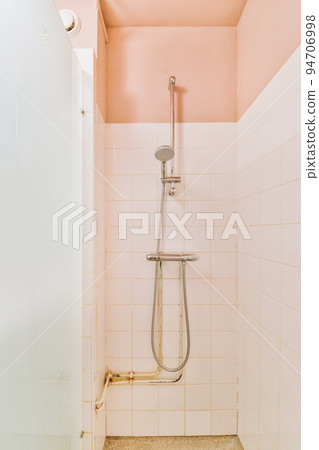 Shower faucets attached to tiled wall near glass partition and ornamental curtail in washroom at home 94706998