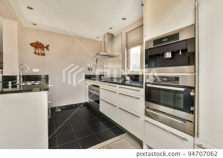 Modern minimalist style interior design of studio apartment with open white kitchen and dining zone with table and chairs illuminated by loft style lamp 94707062