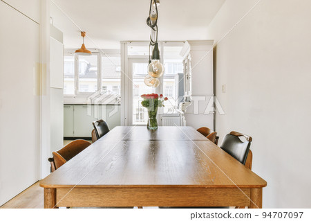 Wooden table with vase of flowers under black pendant lamp in modern living room with sofa near window 94707097