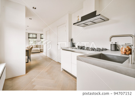 Contemporary minimalist style interior design of light studio apartment with wooden table and chairs in dining zone between open kitchen and living room with white walls and parquet floor 94707152