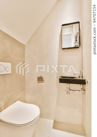 Interior of narrow restroom with sink and wall hung toilet with white walls and checkered floor 94707154