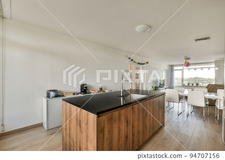 Modern minimalist style interior design of studio apartment with open white kitchen and dining zone with table and chairs illuminated by loft style lamp 94707156
