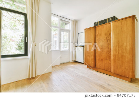 Home interior design of bedroom with bed and wooden wardrobe placed in corner near window in modern apartment 94707173