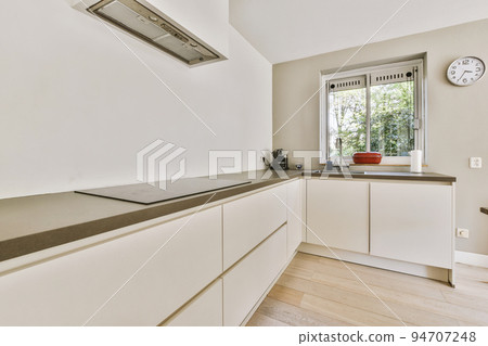 Fragment of interior of light narrow home kitchen with minimalist style white furniture with sink and stove Fragment of interior of light narrow home kitchen with minimalist style white furniture with sink and stove 94707248