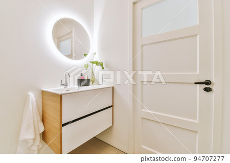 Cupboard with sink and mirror attached to tiled wall near door and drying rack in modern restroom 94707277