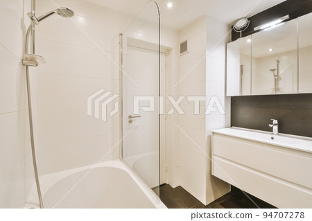 Sinks with mirrors and clean bathtub located near shower box with glass door in modern bathroom with white tiled walls 94707278