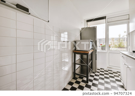 Interior of light kitchen with modern cupboards and appliances located near dining room in modern flat at daytime 94707324