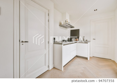 Fragment of interior of light narrow home kitchen with minimalist style white furniture with sink and stove 94707358