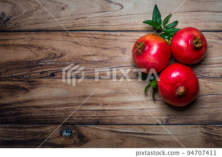 Top view of fresh juicy pomegranates whole and cut, with leaves on a wooden background. Copy space. Concept fresh fruits 94707411