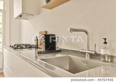 Contemporary open plan kitchen with dining table set and gray sofa in light spacious room Contemporary open plan kitchen with dining table set and gray sofa in light spacious room 94707498