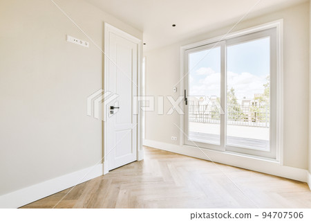 Interior of empty white room with large balcony windows with curtains and wooden parquet floor Interior of empty white room with large balcony windows with curtains and wooden parquet floor 94707506