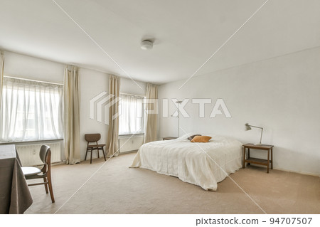 Comfortable bed with white bedclothes and bedside table with lamp placed near window in light bedroom at home Comfortable bed with white bedclothes and bedside table with lamp placed near window in light bedroom at home 94707507
