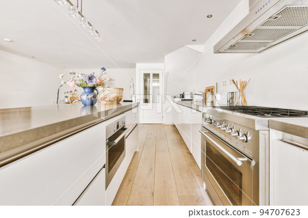 Modern minimalist style interior design of studio apartment with open white kitchen and dining zone with table and chairs illuminated by loft style lamp 94707623