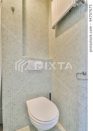 Wall hung toilet and small sink in corner in lavatory room with beige tile 94707675