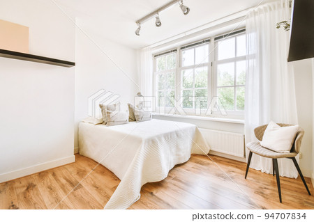 Home interior design of bedroom with bed and wooden wardrobe placed in corner near window in modern apartment 94707834