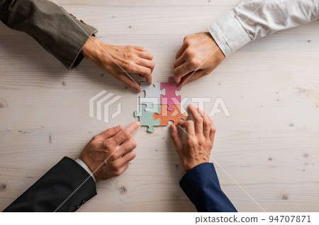 Hands of four businesspeople joining matching puzzle pieces 94707871