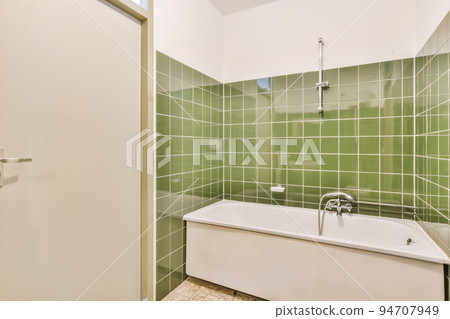 Bathtub with glass shower placed in corner near sink with toilet in small light bathroom with white tile walls Bathtub with glass shower placed in corner near sink with toilet in small light bathroom with white tile walls 94707949