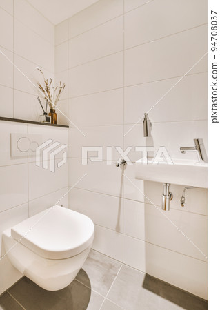 Interior of narrow restroom with sink and wall hung toilet with white walls and checkered floor Interior of narrow restroom with sink and wall hung toilet with white walls and checkered floor 94708037