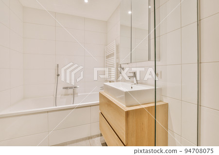 Sinks with mirrors and clean bathtub located near shower box with glass door in modern bathroom with white tiled walls 94708075
