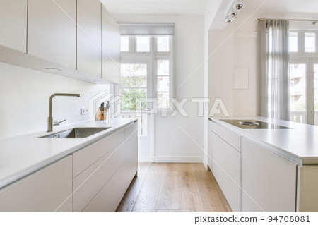 Interior of spacious light kitchen with modern white furniture and pop art portrait in light apartment Interior of spacious light kitchen with modern white furniture and pop art portrait in light apartment 94708081