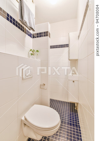 Interior of narrow restroom with sink and wall hung toilet with white walls and checkered floor 94708084