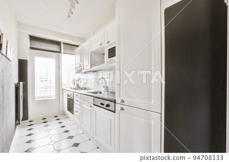 Light small home kitchen with wide window furnished with cupboards and shelves with appliances in modern urban apartment 94708133