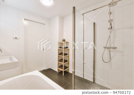 Sinks with mirrors and clean bathtub located near shower box with glass door in modern bathroom with white tiled walls Sinks with mirrors and clean bathtub located near shower box with glass door in modern bathroom with white tiled walls 94708172