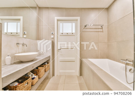 Sinks with mirrors and clean bathtub located near shower box with glass door in modern bathroom with white tiled walls Sinks with mirrors and clean bathtub located near shower box with glass door in modern bathroom with white tiled walls 94708206
