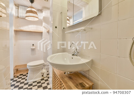 Wall hung toilet and small sink in corner in lavatory room with beige tile 94708307