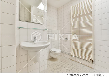 Wall hung toilet and small sink in corner in lavatory room with beige tile Wall hung toilet and small sink in corner in lavatory room with beige tile 94708329