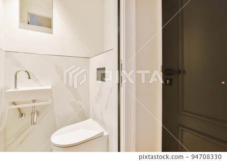 Interior of narrow restroom with sink and wall hung toilet with white walls and checkered floor Interior of narrow restroom with sink and wall hung toilet with white walls and checkered floor 94708330
