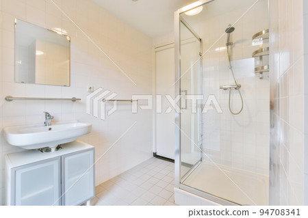 Interior of modern bathroom with rectangular mirror and clean sinks attached to white tiled wall near shower box in modern washroom Interior of modern bathroom with rectangular mirror and clean sinks attached to white tiled wall near shower box in modern washroom 94708341