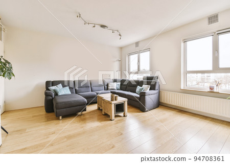 Simple interior of light living room with gray sofa in front of TV and dining table against window Simple interior of light living room with gray sofa in front of TV and dining table against window 94708361