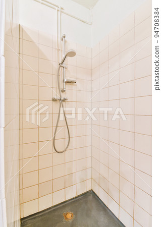 Shower faucets attached to tiled wall near glass partition and ornamental curtail in washroom at home Shower faucets attached to tiled wall near glass partition and ornamental curtail in washroom at home 94708384