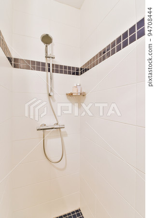 Shower faucets attached to tiled wall near glass partition and ornamental curtail in washroom at home Shower faucets attached to tiled wall near glass partition and ornamental curtail in washroom at home 94708444