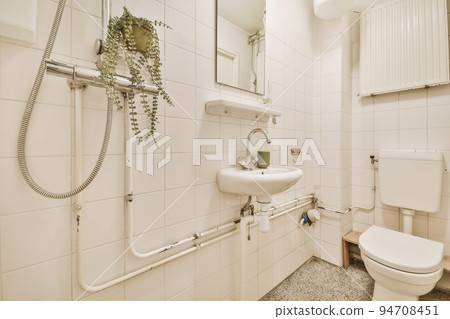 Interior of narrow restroom with sink and wall hung toilet with white walls and checkered floor 94708451