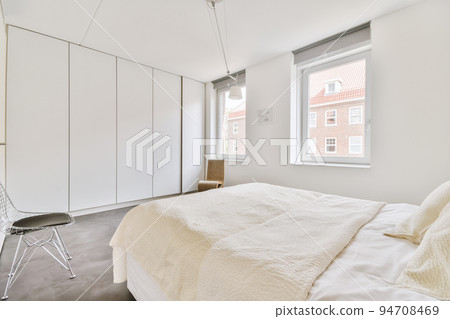 Home interior design of bedroom with bed and wooden wardrobe placed in corner near window in modern apartment Home interior design of bedroom with bed and wooden wardrobe placed in corner near window in modern apartment 94708469
