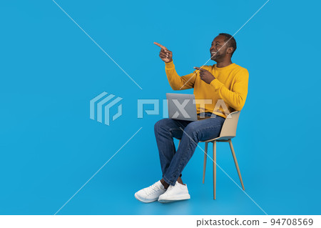 Cheerful black man sitting on chair with laptop, copy space Cheerful black man sitting on chair with laptop, copy space 94708569