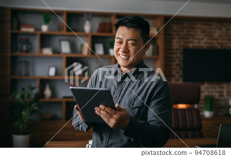 Smiling successful mature korean man typing on tablet, chatting with client, analyze startup data in office interior Smiling successful mature korean man typing on tablet, chatting with client, analyze startup data in office interior 94708618