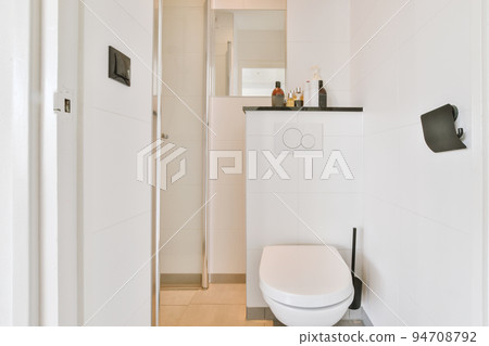 Interior of narrow restroom with sink and wall hung toilet with white walls and checkered floor Interior of narrow restroom with sink and wall hung toilet with white walls and checkered floor 94708792