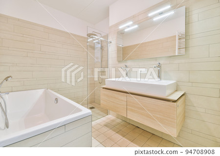 Sinks with mirrors and clean bathtub located near shower box with glass door in modern bathroom with white tiled walls 94708908