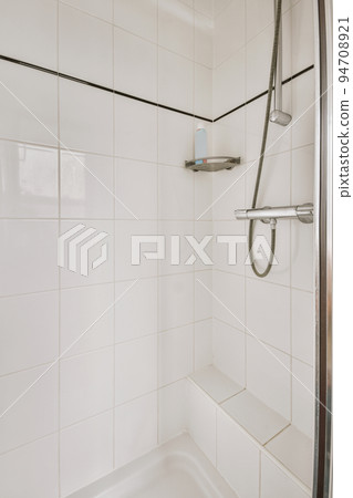 Shower faucets attached to tiled wall near glass partition and ornamental curtail in washroom at home 94708921